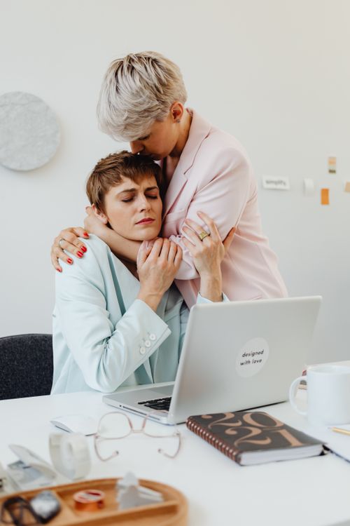 Free Two women share a comforting hug in a modern office setting. Stock Photo