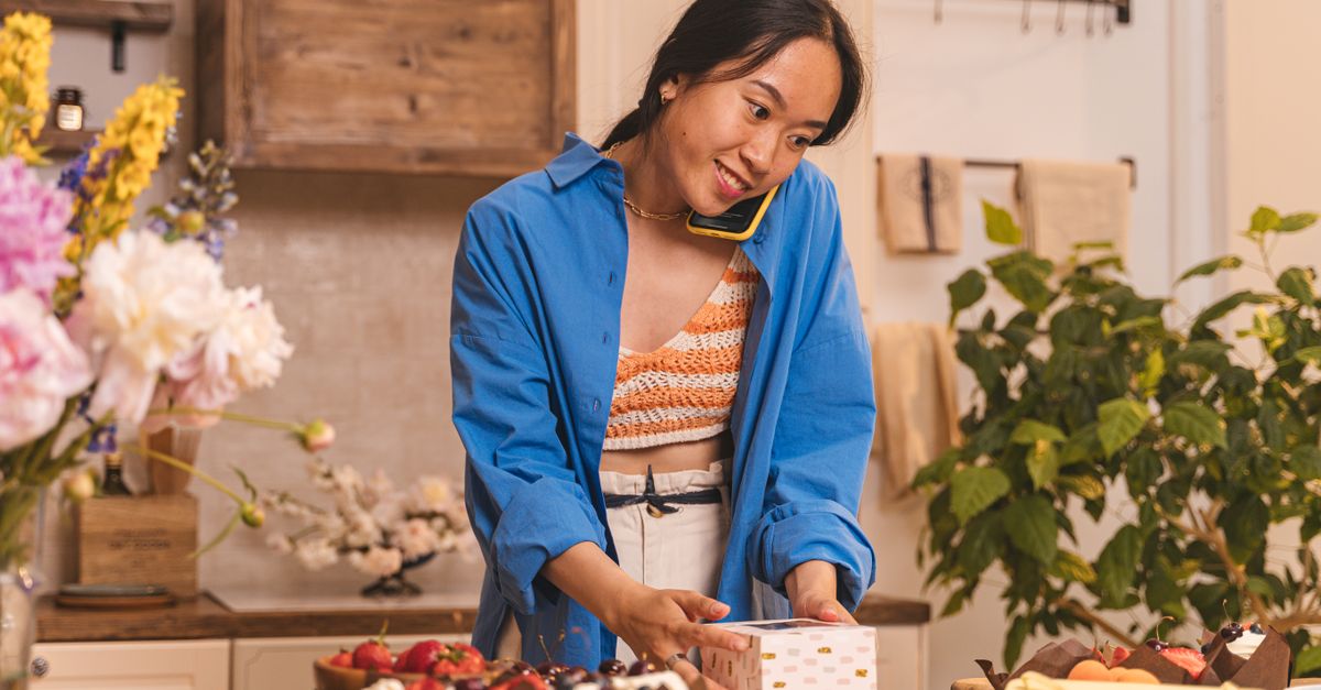 Donna al telefono mentre sistema dolci in una scatola