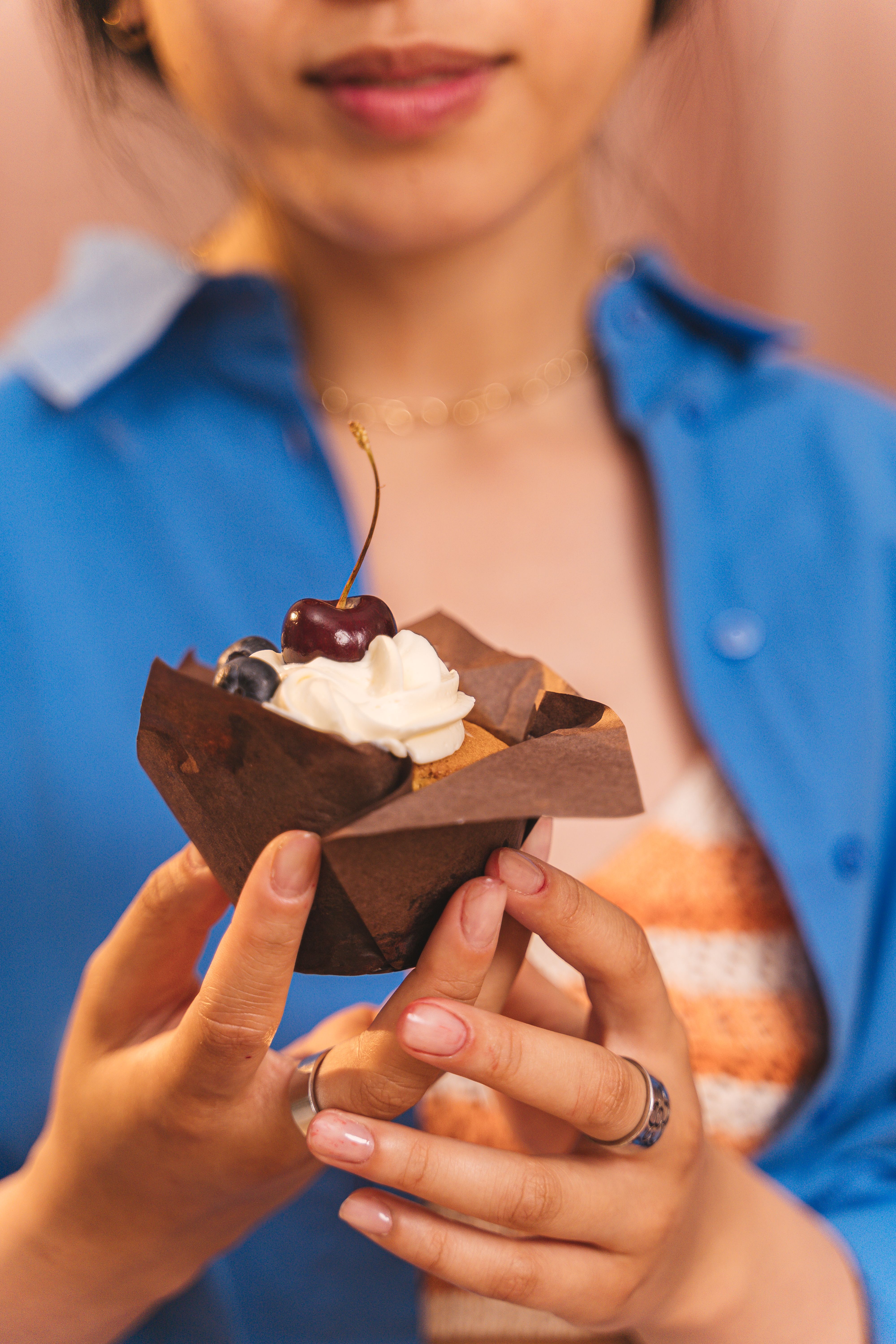 A woman holding a beautifully decorated cupcake with cream and a cherry on top.