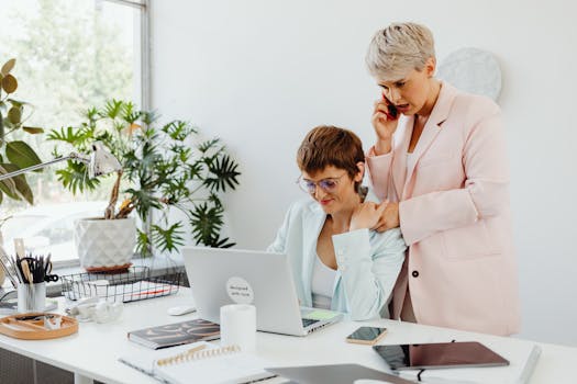 Lesbian couple working together in a bright office with computer and phone.