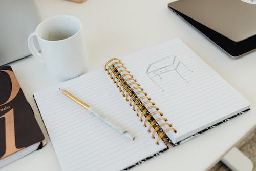 Free A Mug Beside a Notebook with a Sketch Stock Photo