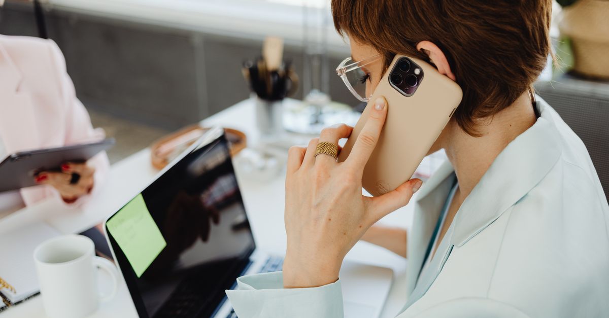 A businesswoman using a smartphone beside her laptop in an office.