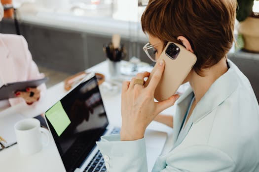 A businesswoman multitasking between a smartphone and laptop in an office setting efficiently.
