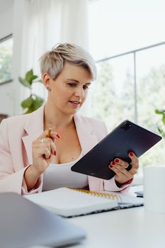 A focused professional woman using a tablet at her desk in a well-lit modern office setting.