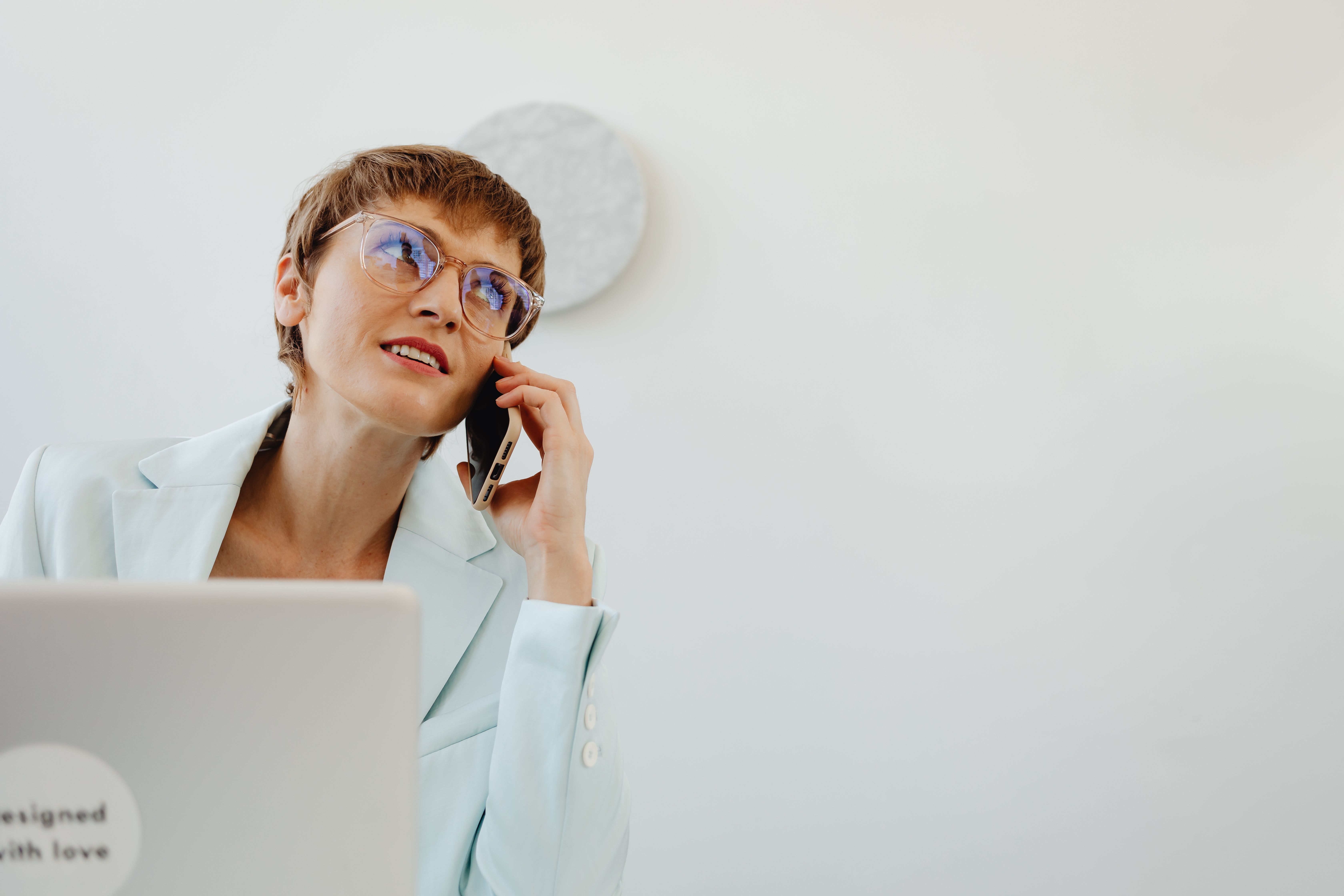 Femme dans un cadre de bureau, portant des lunettes, parlant sur un smartphone, et dégageant du professionnalisme.