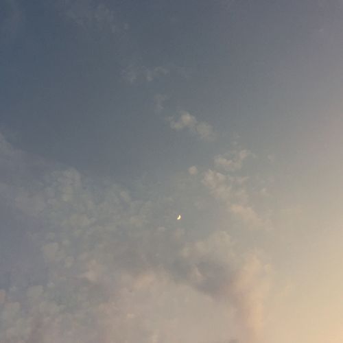 Free A serene view of a crescent moon amidst soft clouds during twilight. Stock Photo