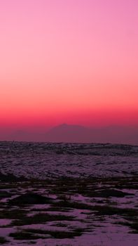 A tranquil snowy terrain under a vibrant pink and orange dusk sky.