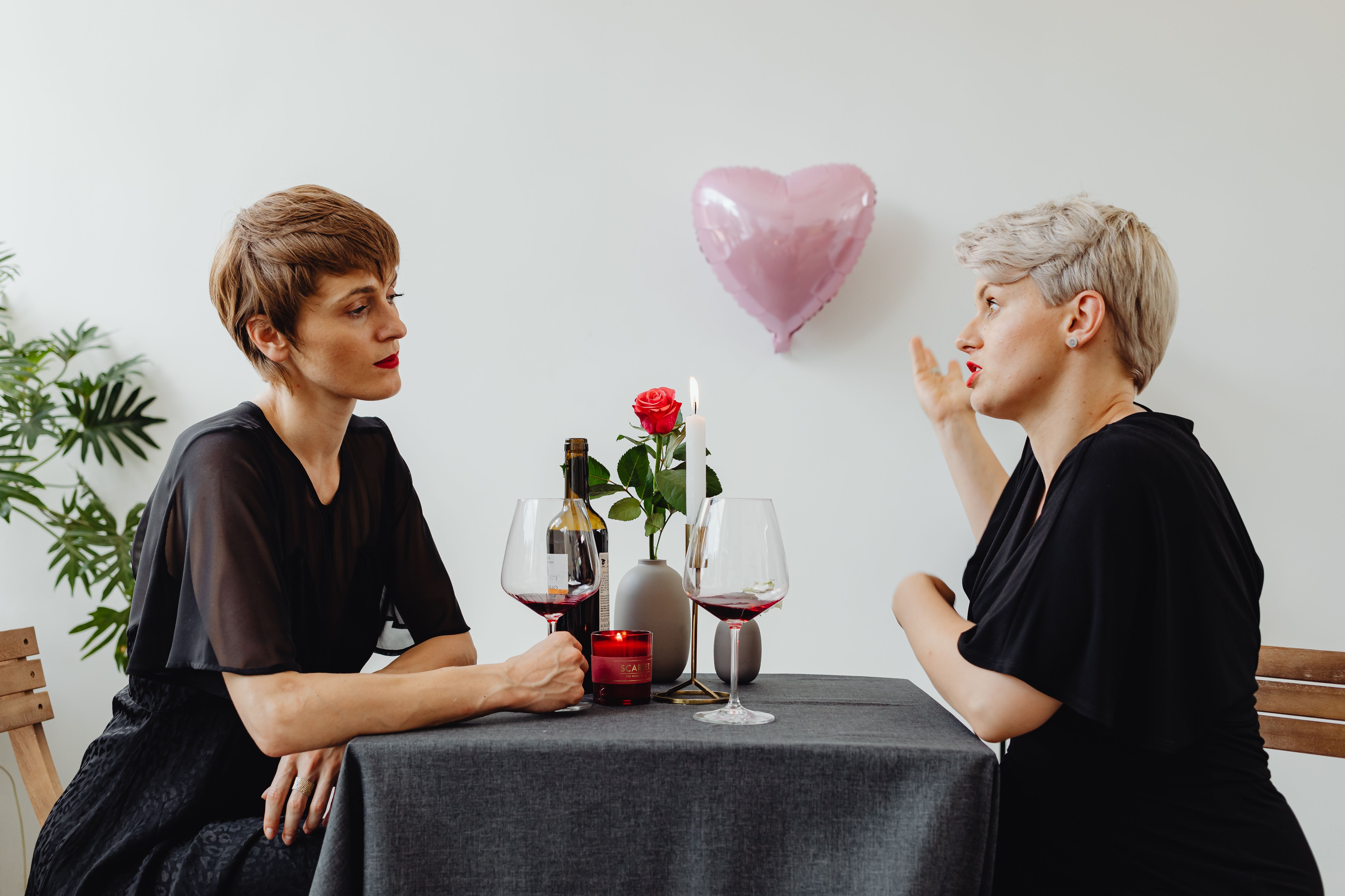 Two women enjoying a romantic dinner with red wine and candles indoors.