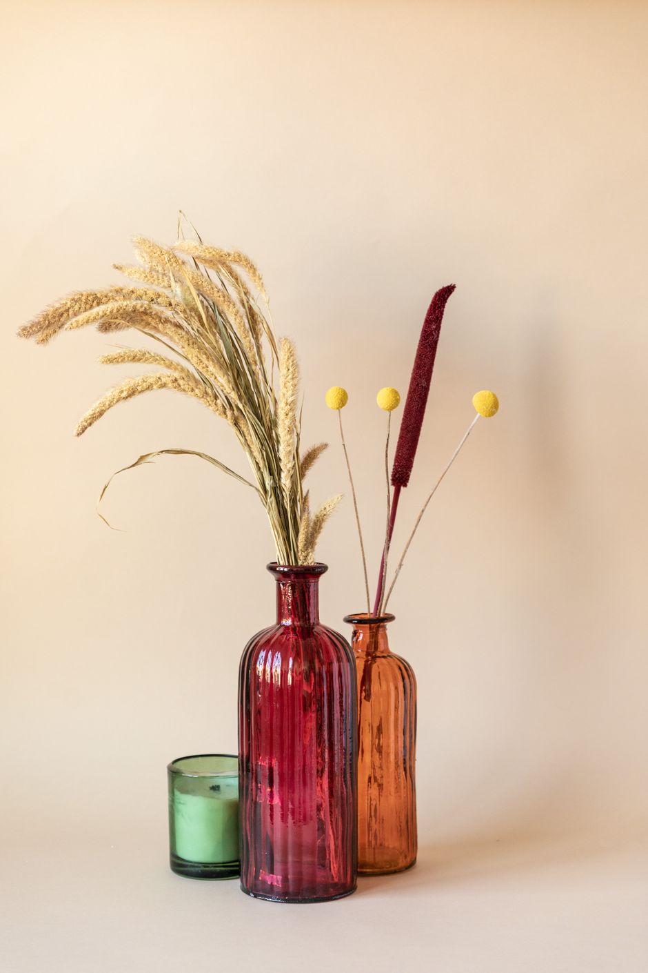 Coloured glass bottles with dried grasses on a warm backdrop — photo by RDNE Stock project on Pexels