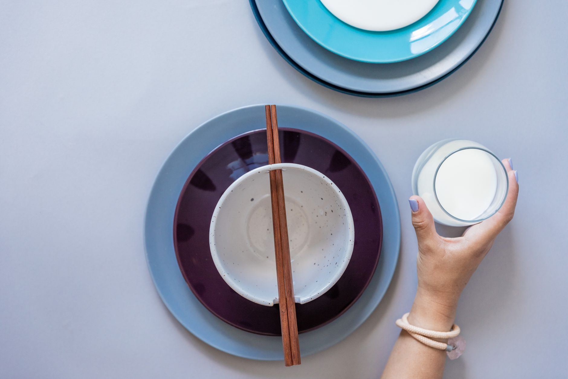 Top view of colorful plates and a hand holding a glass of milk with chopsticks.