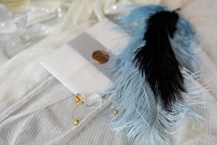 Black And Blue Feather Beside An Invitation Card On A White Surface