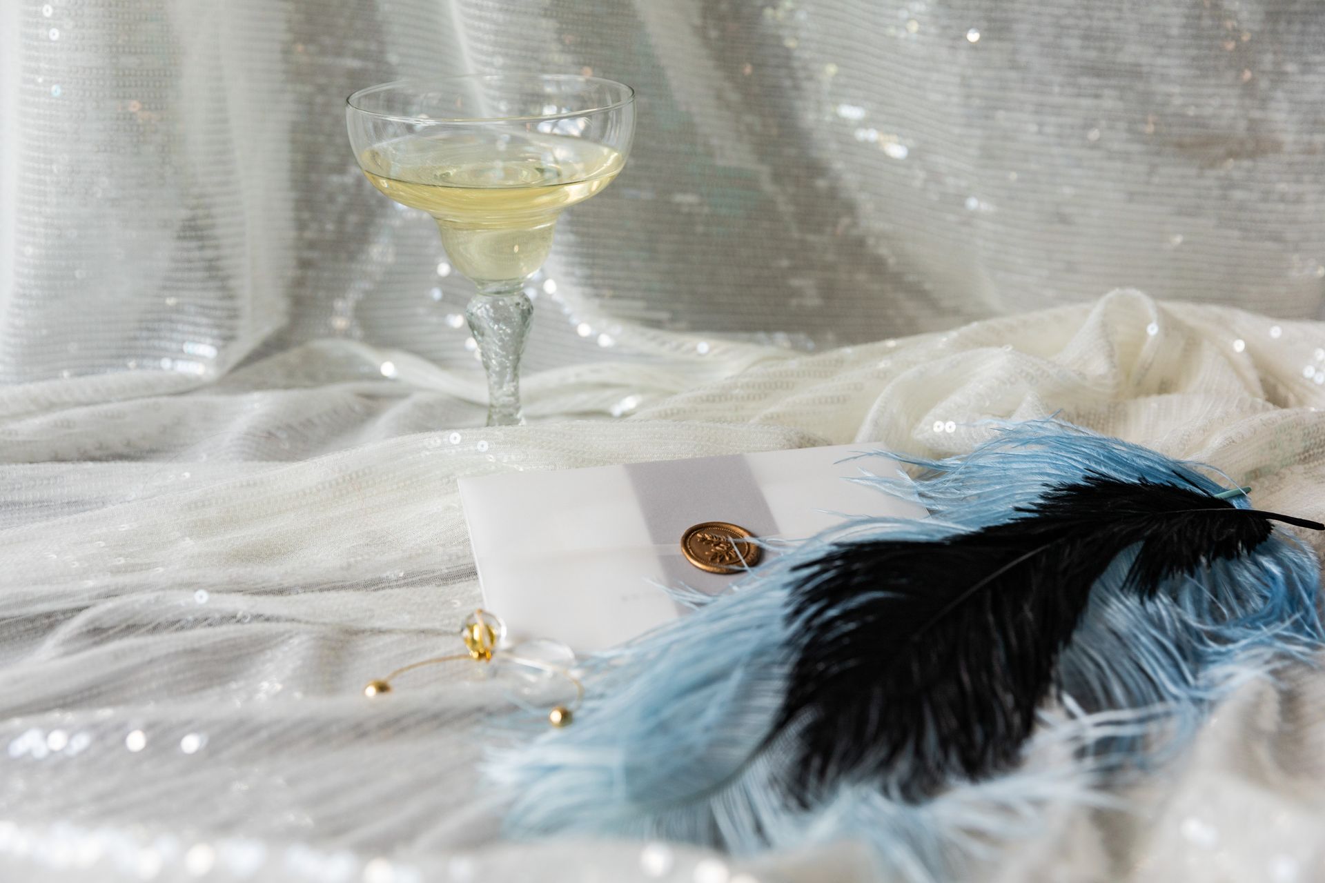 Stylish Art Deco themed flat lay with feathers, invitation, and champagne flute.