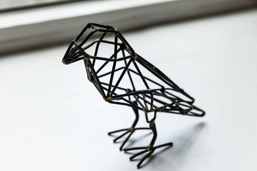 Sleek black metal geometric bird sculpture perched on a bright windowsill.