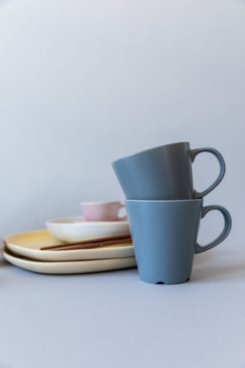 Free Elegant arrangement of ceramic cups and plates on a neutral gray surface, showcasing minimalist dinnerware design. Stock Photo