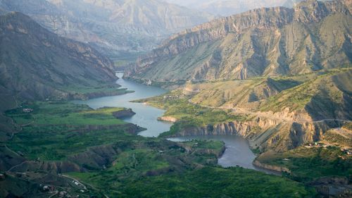 Free A picturesque aerial view of a winding river cutting through lush green valleys and rugged mountains. Stock Photo