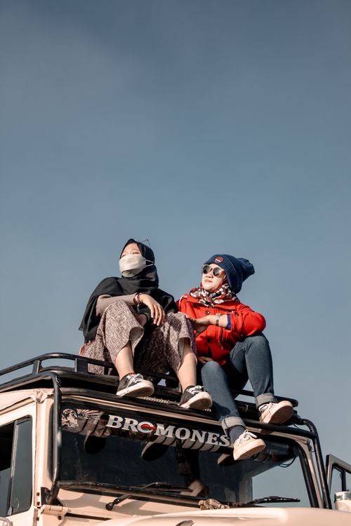 Free Two women sitting on a jeep roof, enjoying a sunny day in East Java, Indonesia, capturing the spirit of adventure. Stock Photo