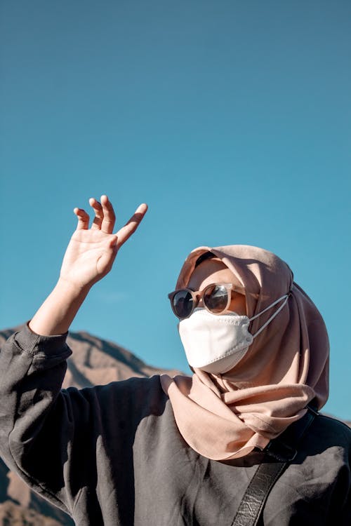 Free Woman in Pink Hijab and Sunglasses Wearing Face Mask while Looking Afar Stock Photo