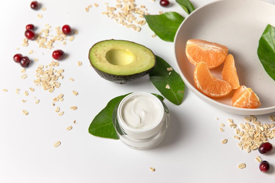 Fresh avocado, cream, and fruits on a white surface for skincare and healthy eating.