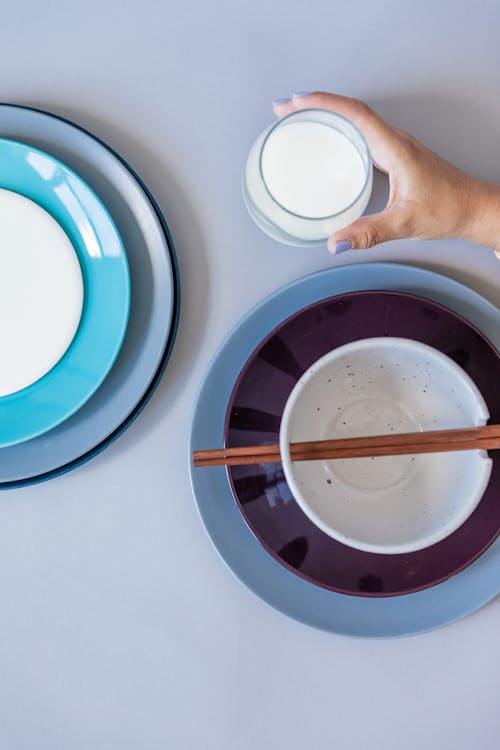 Person Holding Glass Beside Ceramic Plates and Bowl with Chopsticks