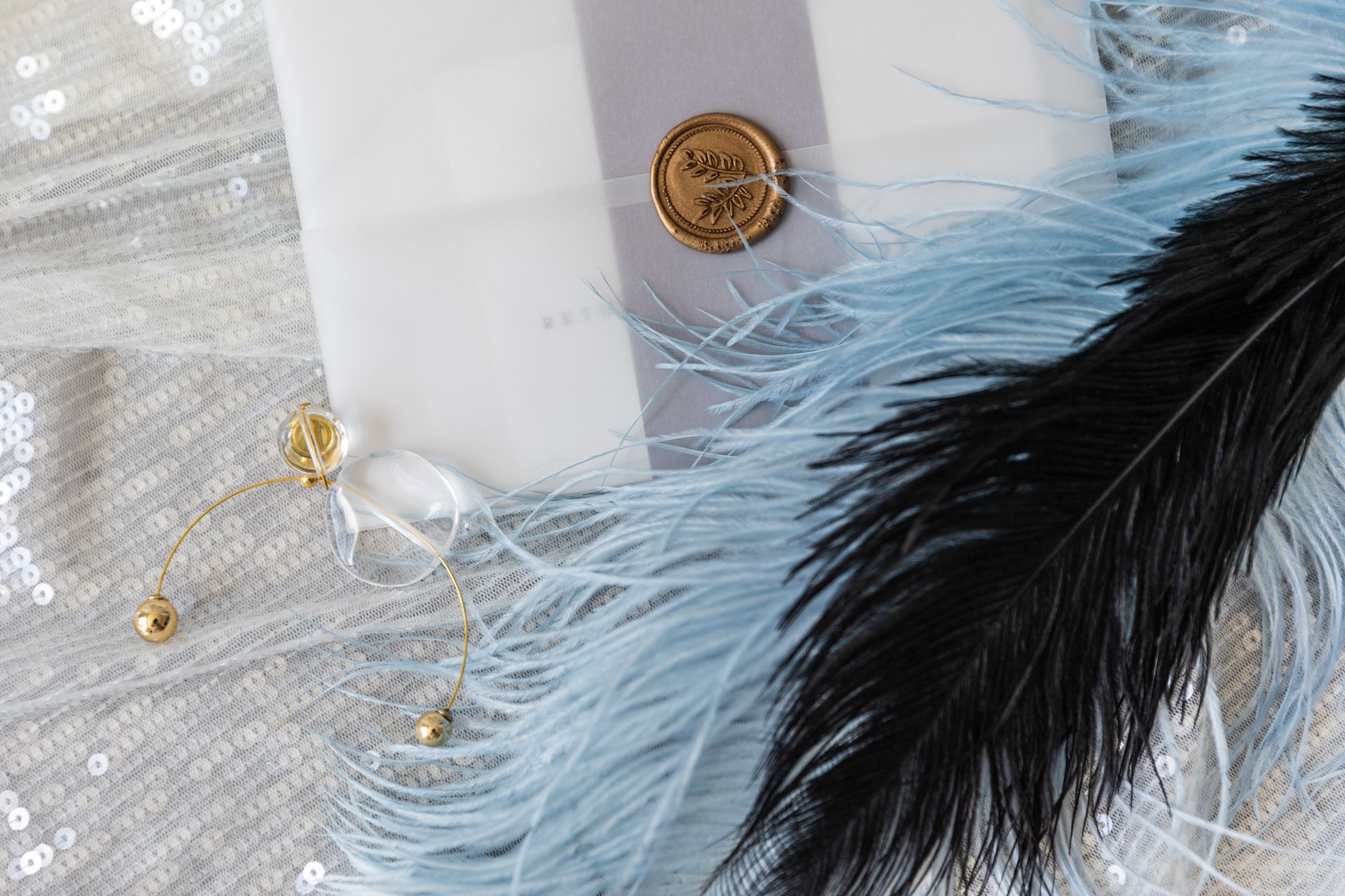 Faire-part chic avec détails dorés, plumes et paillettes posés sur une table, ambiance élégante et chaleureuse
