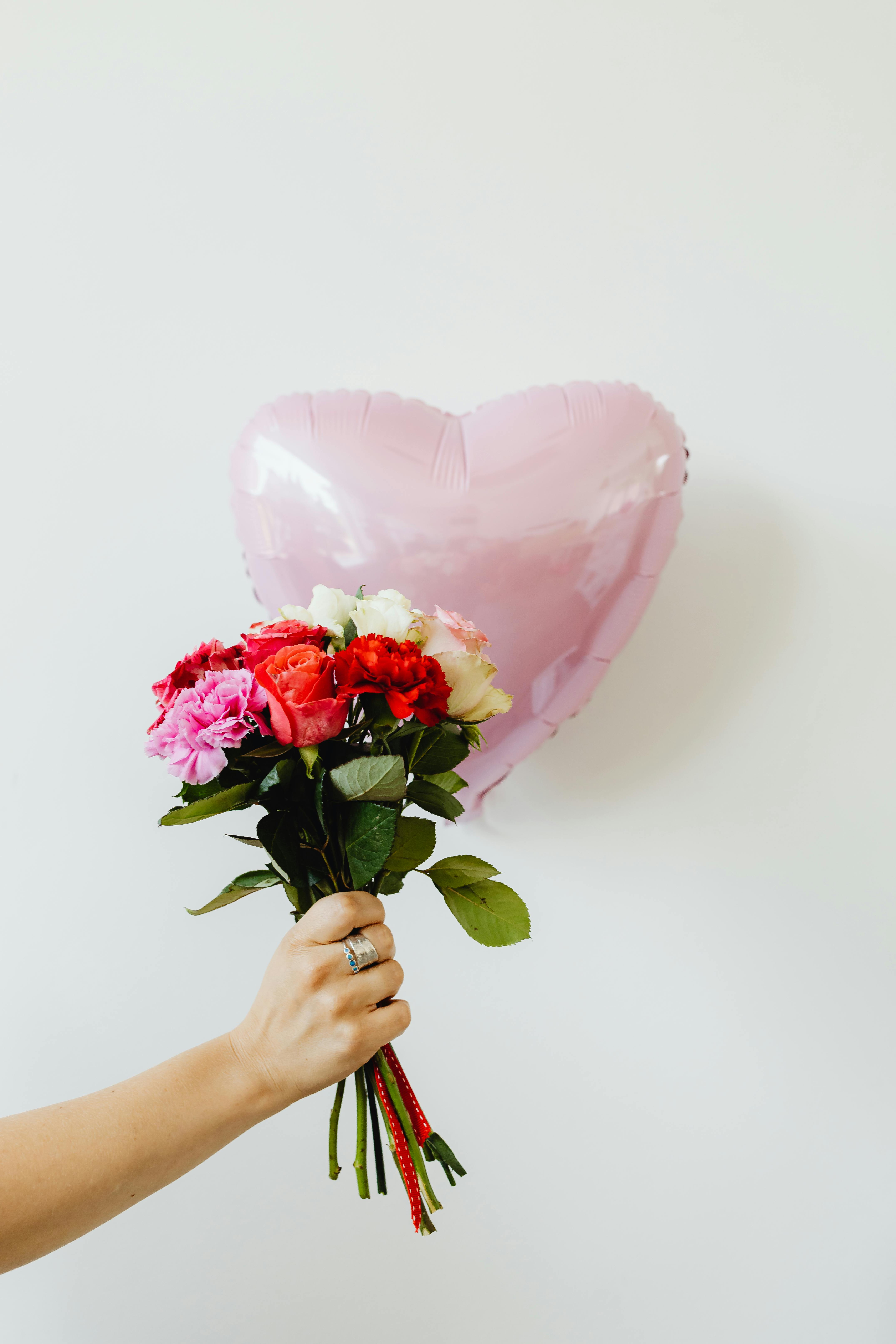 hand holding a bunch of flowers and pink balloon