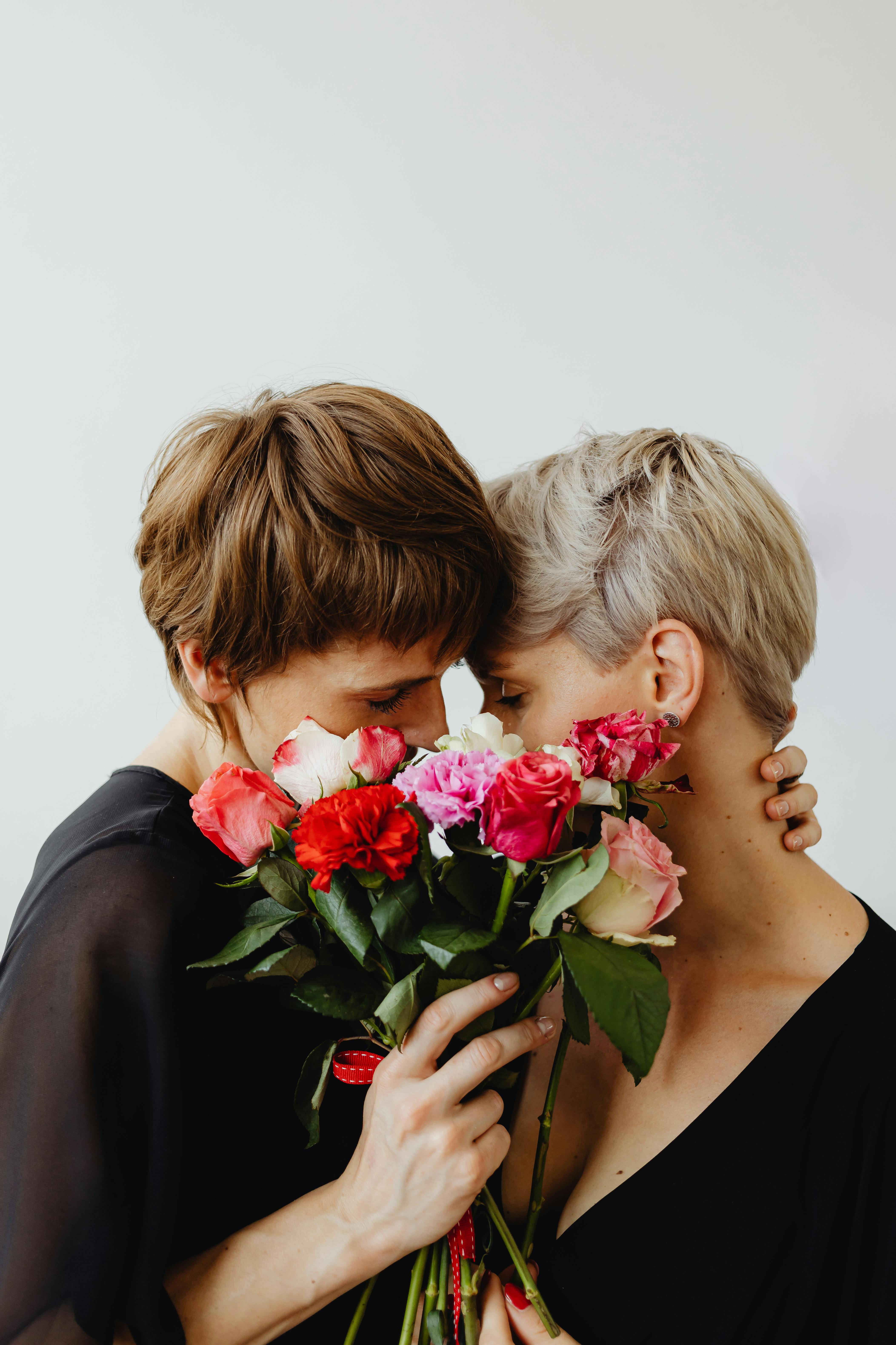Two women sharing an intimate moment with a bouquet, symbolizing love and connection.