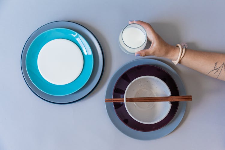 Hand Holding A Glass Of Milk By Plates And A Bowl On A Table