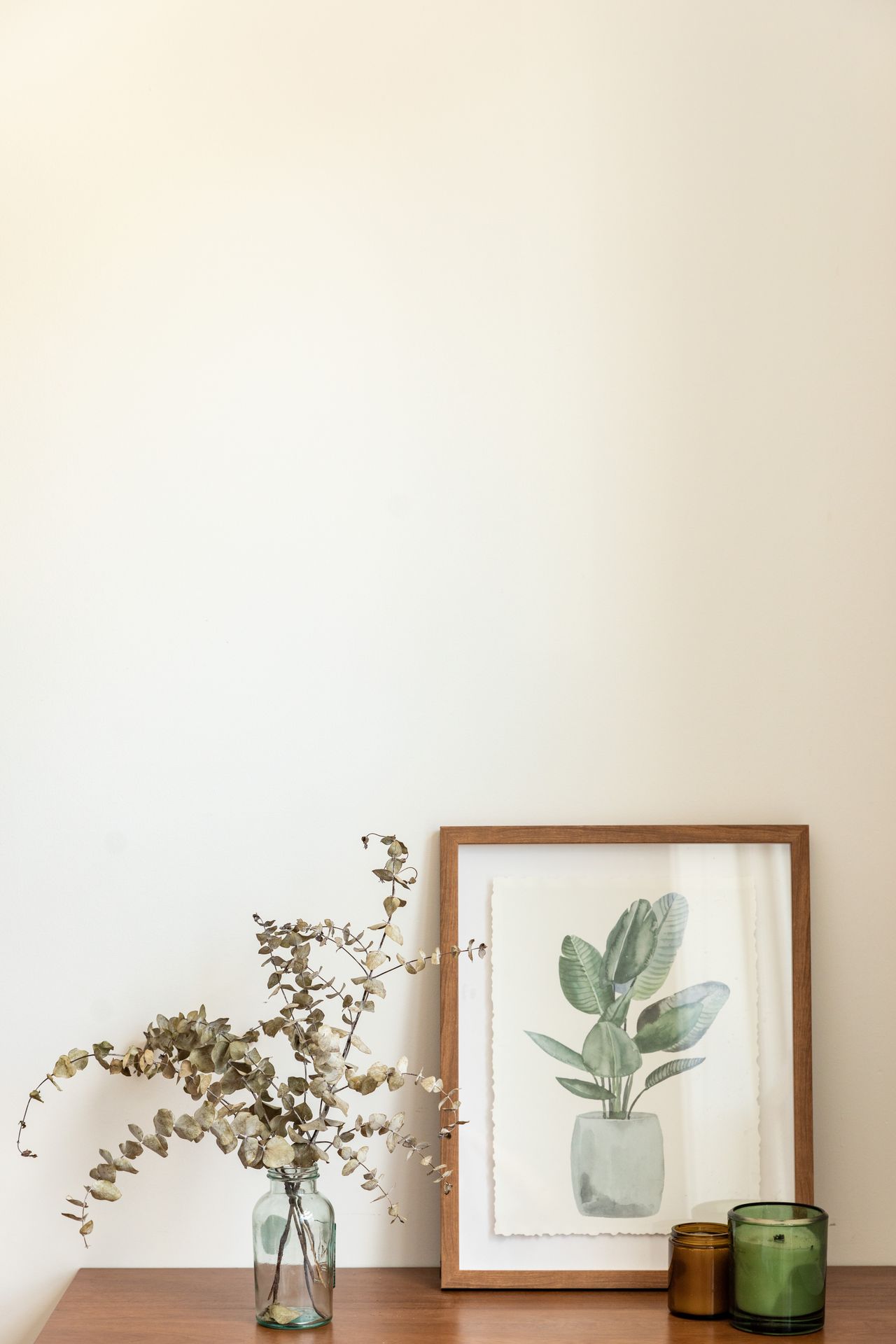 Wooden tabletop styled with a framed print, dried stems, and candles