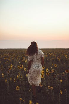 Peaceful scene of woman walking through a sunflower field during twilight, exuding tranquility.