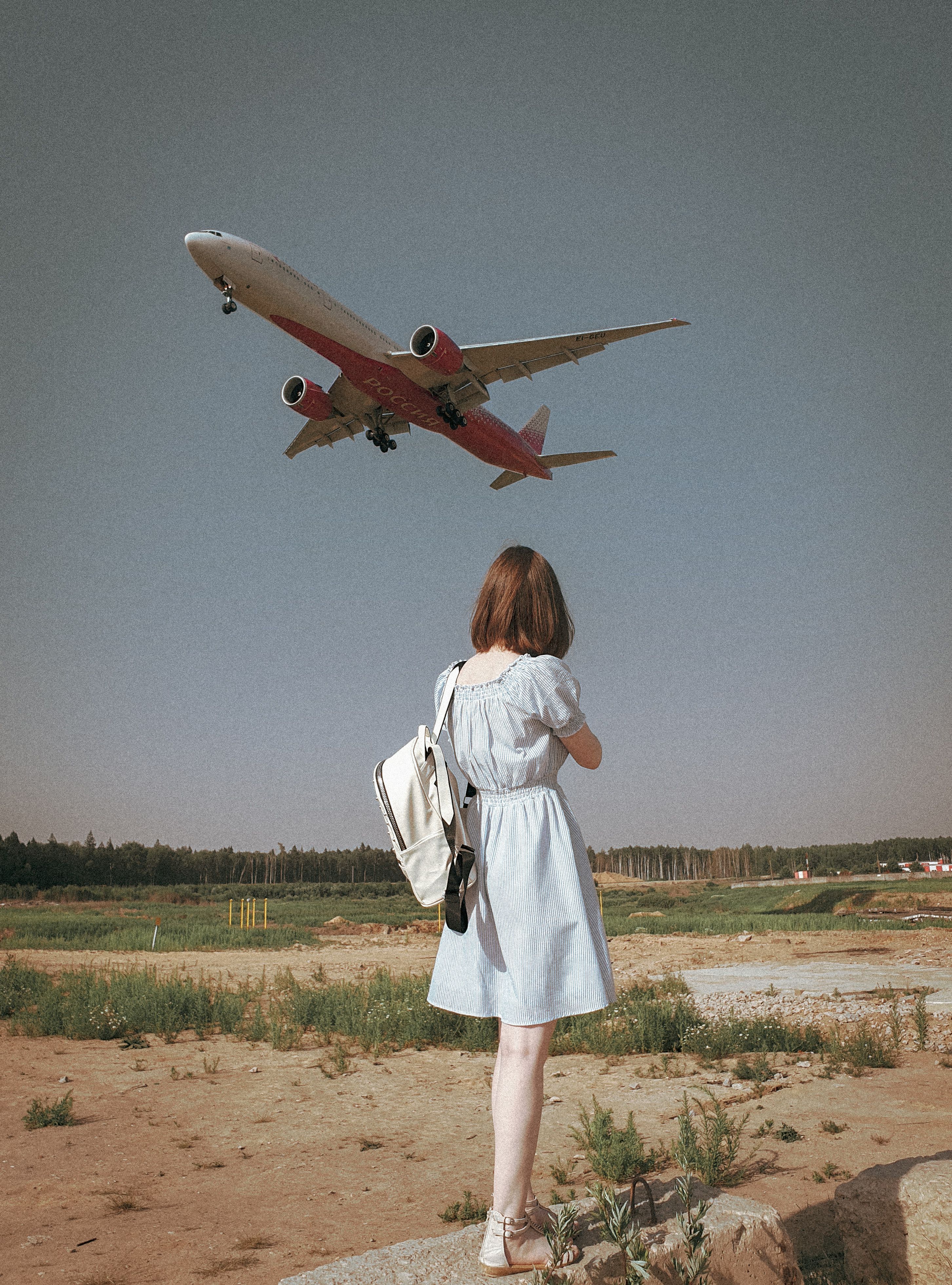 A woman watches from below as an airplane flies overhead against a clear sky.