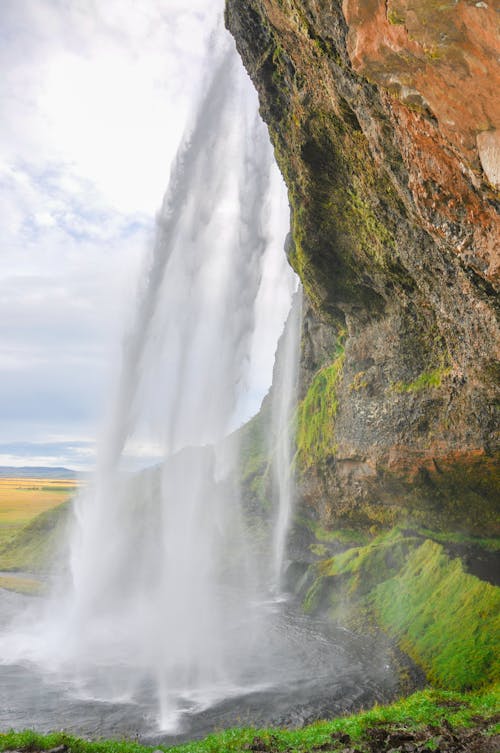 Waterfalls on Brown Rocky Mountain Under White Cloudy Sky