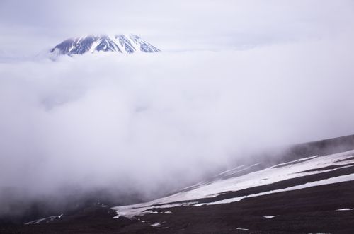 Free A majestic snow-capped mountain peak rises through thick clouds, creating a serene winter landscape. Stock Photo