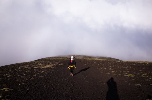 A lone hiker explores a rugged mountain terrain under a cloudy sky, embodying adventure.