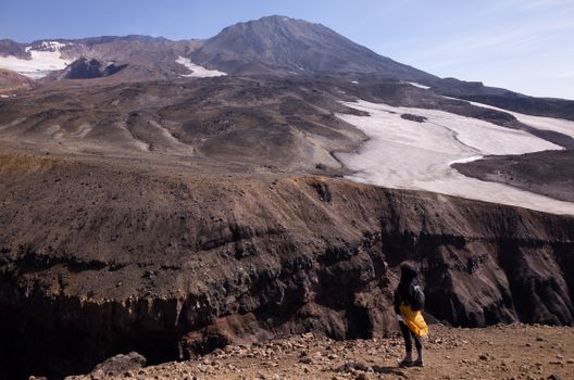 A woman hiker stands at a volcanic crater's edge, embracing adventure and nature.