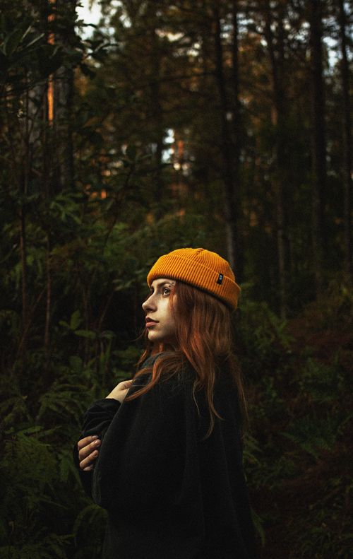 Free Young woman wearing a yellow beanie amidst a dense forest setting, captured in a moody, artful style. Stock Photo