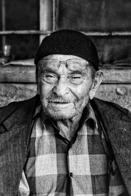 Free A close-up black and white portrait of an elderly man wearing eyeglasses and a plaid shirt, smiling softly. Stock Photo