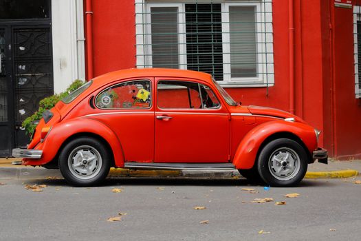 Classic red Volkswagen Beetle parked by a vibrant red building on city street.