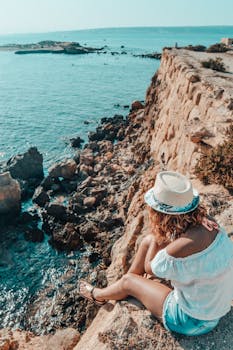 Woman enjoys the sunny view from a rocky cliff by the sea in Alacant, Spain.