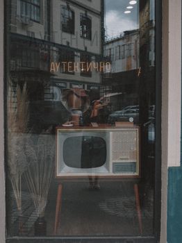 A vintage television set displayed in a shop window with reflections of the street outside.