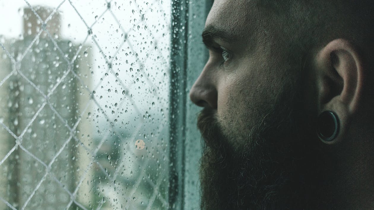 Free Selective Focus Photography of Man Staring on Glass Window Filled With Droplets Stock Photo