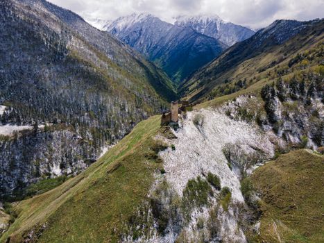 Stunning aerial view of snow-dusted mountains and ancient ruins in a lush valley.