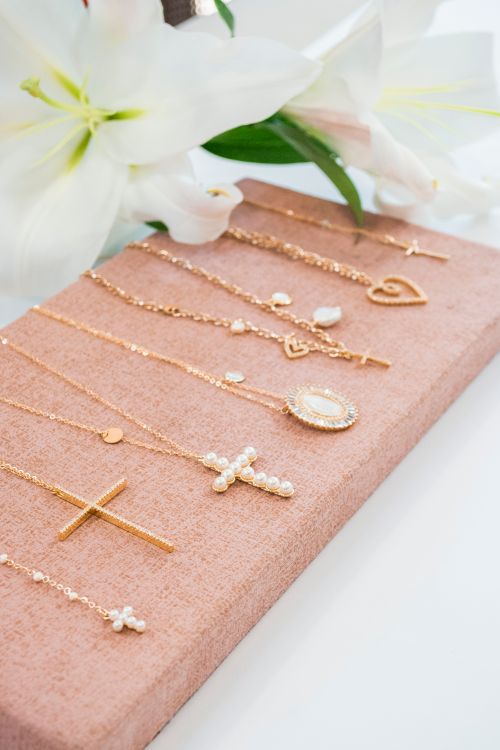 Free Elegant gold and pearl pendants arranged on pink fabric with white lilies in the background. Stock Photo