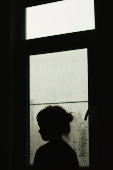 A dark silhouette of a child by a window creates a dramatic and moody atmosphere.