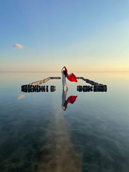 A woman stands gracefully on a reflective water surface at sunrise, embracing tranquility.