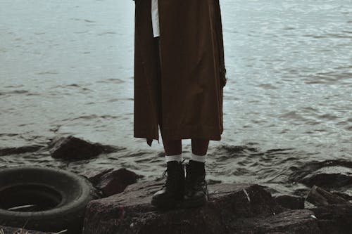 Person in Black Boots Standing on Rocks Near Sea