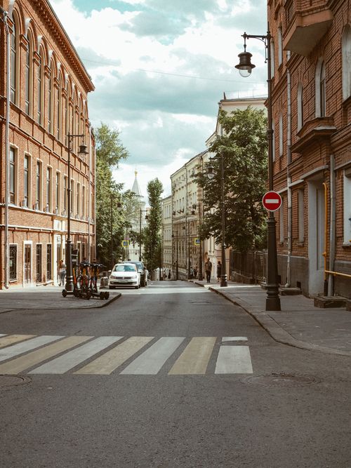 Free Street view in Moscow showing historic brick buildings, parked cars, and a zebra crossing on a clear day. Stock Photo