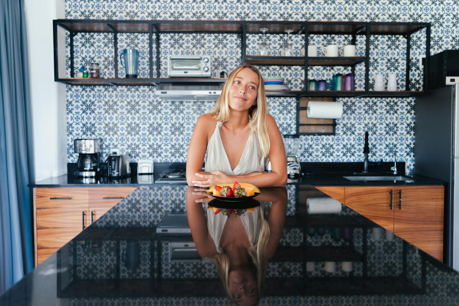 Woman in kitchen smiling over healthy breakfast plate, showcasing modern interior design