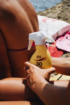 Woman applying SPF 30 sunscreen on beach for sun protection and skincare.