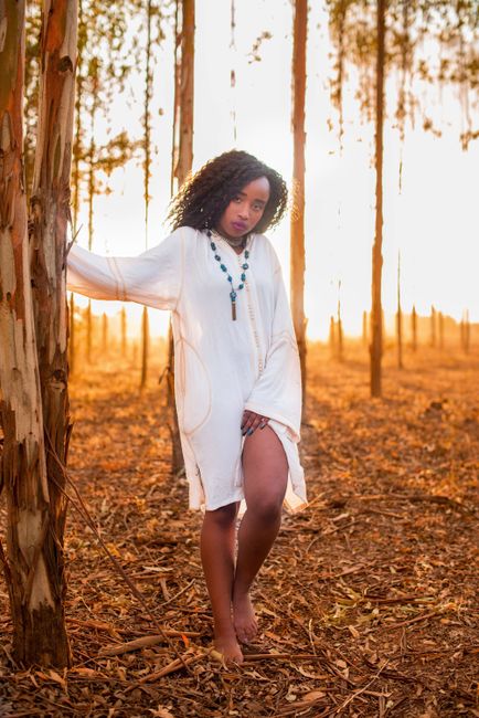 Captivating portrait of a young woman in a white dress amidst a sunlit forest during sunset.