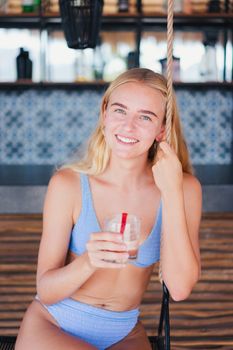 Young woman in bikini enjoying a refreshing drink on a sunny day.